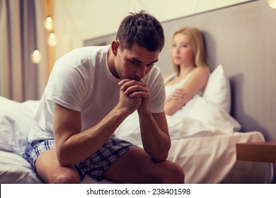 Hotel, Travel, Relationships, And Sexual Problems Concept - Upset Man Sitting On The Bed With Woman On The Back