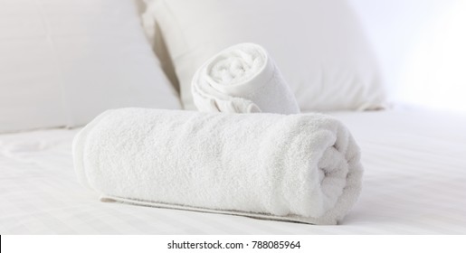 Hotel's Bedroom. White Fluffy, Rolled Towels, Linen Sheets And Pillows On A Tidy Bed. Close Up View.