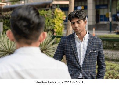 A hotheaded young indian man stares down his workmate while outside the office. Animosity in the workplace. - Shutterstock ID 2311326501