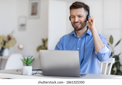 Hotline Operator. Handsome Young Man Customer Support Manager In Headset Working With Laptop Computer In Office, Consulting Clients Online, Managing Issues, Sitting At Desk, Free Space