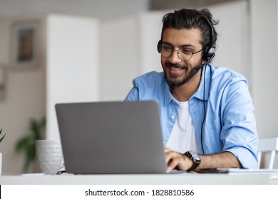 Hotline Operator. Portrait Of Indian Customer Support Manager Man In Headset Working With Laptop Computer In Office, Consulting Clients, Western Guy Sitting At Desk And Smiling, Free Space - Shutterstock ID 1828810586