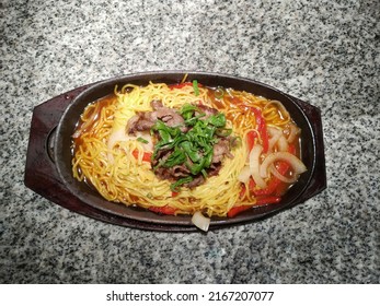 A hotplate contains ramen noodle with beef, peppers and onions
