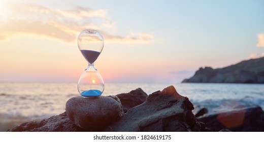 Hourglass with blue falling sand inside. Ocean landscape and golden hour. Time fly and need in rest concept, copy space