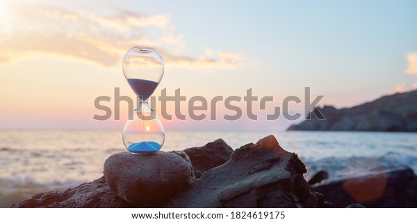 Hourglass\
with blue falling sand inside. Ocean landscape and golden hour.\
Time fly and need in rest concept, copy\
space