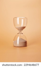 Hourglass with clean sand pouring down countdown the time, isolated on the bright solid fond plain sandy beige background - Shutterstock ID 2294648677