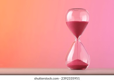 Hourglass with flowing pink sand on table against color background. Space for text - Powered by Shutterstock