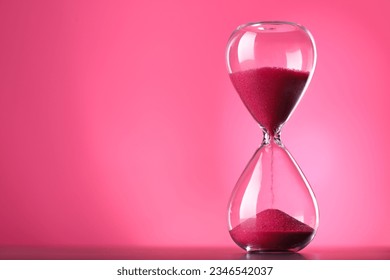 Hourglass with flowing sand on table against pink background, space for text