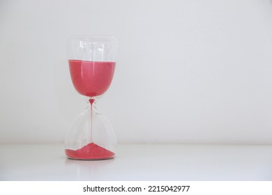 An Hourglass Isolated On Left Of White Background, Red Sand Slipping Away, Measuring Passage Of Time, Running Out Of Time Concept