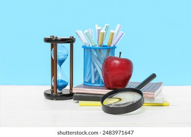 Hourglass, magnifying glass, different school supplies and red apple on table against blue background - Powered by Shutterstock