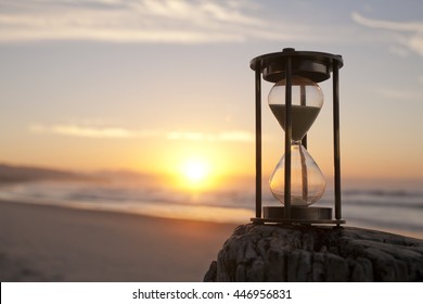 An hourglass on a beach in front of a beautiful sunrise, focus on hourglass.