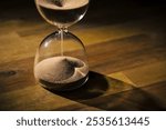 Hourglass on a wooden table with a black background, sand flowing through the bulb. Time, and life journey concepts.