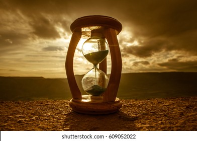 Hourglass Passing of Time Lapse Clouds. An hourglass in front of a bright blue sky with puffy white clouds passing. Time concept. Sunset time
