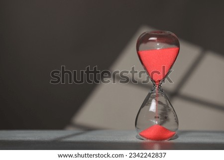 Hourglass with red flowing sand on table against light grey background, space for text