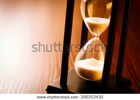 Hourglass with the sand running through in a wood frame on a wooden surface with shine and copyspace