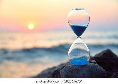Hourglass with sand standing on rock. Sunset over sea and nature landscape. Running of time and relax idea, copy space - Shutterstock ID 1823676704