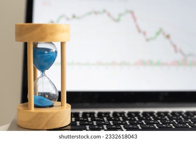 Hourglass and stacks of gold coins on the background of financial charts and graphs.  - Powered by Shutterstock
