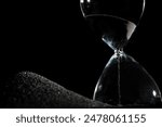 Hourglass stand on black sand with silhouette shadow over black background. Black hourglass show more time Deadline extended time management hope concept hour glass, life clock passing by