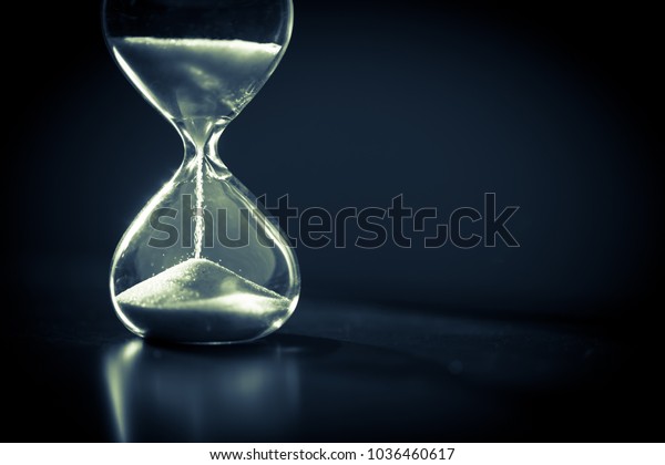 Hourglass as time passing concept for business\
deadline, urgency and running out of time. Sandglass, egg timer on\
dark background showing the last second or last minute or time out.\
 With copy space.