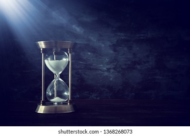 Hourglass as time passing concept in front of black wall background. Conceptual photo on history, fantasy and education.