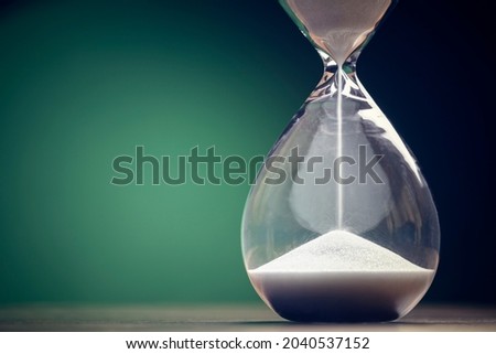 Hourglass time passing green background concept for business deadline, urgency and running out of time