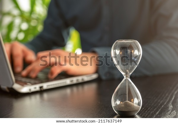 Hourglass with time running out in an office as a\
symbol of time pressure at\
work
