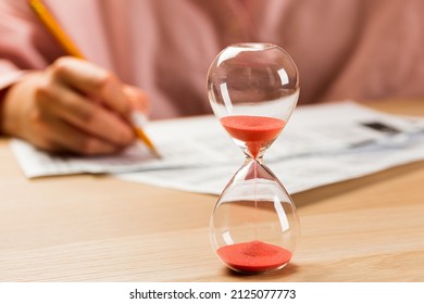 Hourglass with time running out and student hand testing in exercise and passing exam carbon paper computer sheet with pencil in school test room
