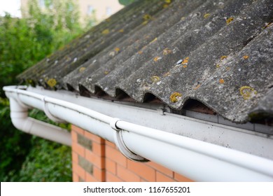 House asbestos roof with close up gutter holder and plastic roof gutter pipe. Guttering.