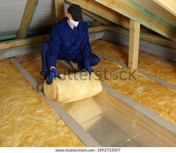 House attic insulation - construction worker installing\
glass wool 