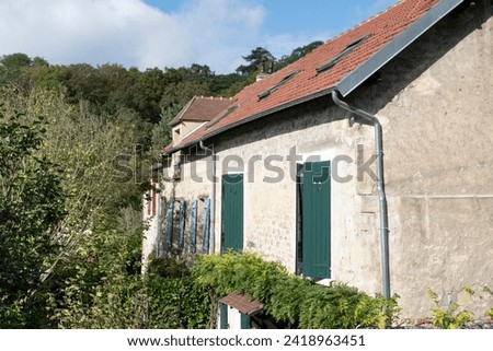 House in Auvers-sur Oise in France with weathered plastered walls and windows with different colored shutters, red, blue and green