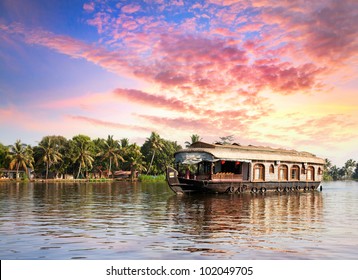 House boat in backwaters near palms at dramatic sunset sky in alappuzha, Kerala, India