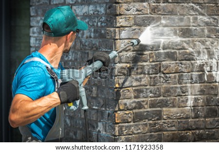 House Brick Wall Washing Using Pressure Washer. Caucasian Worker in His 30s.