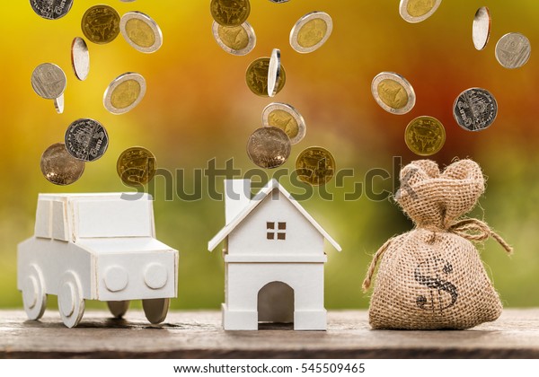 A house and car model and money\
bag with gold coins dropping on the top for loans\
concept.