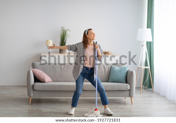 House cleaning\
with fun. Happy housewife singing her favorite song during cleanup,\
using mop as microphone, enjoying domestic work. Positive young\
maid tidying her home with\
pleasure