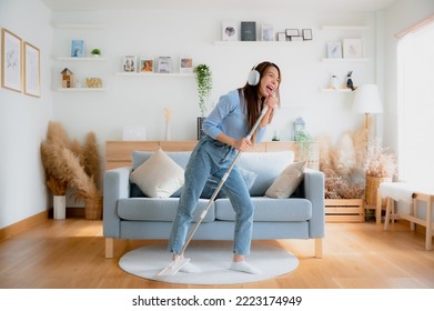 House cleaning with fun. Happy young asian housewife singing her favorite song during cleanup, using mop as microphone, enjoying domestic work. Young woman dancing and cleaning in living room - Shutterstock ID 2223174949