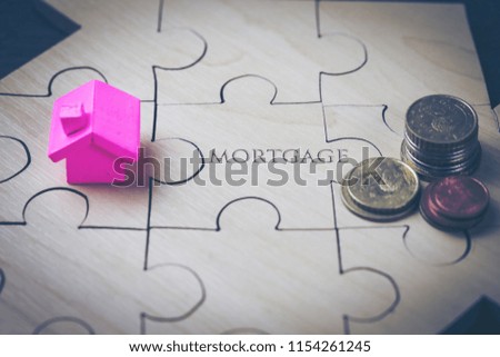 The house and coins are placed on a piece of puzzles with last piece with text mortgage. concept real estate investment for saving or investment for a house.