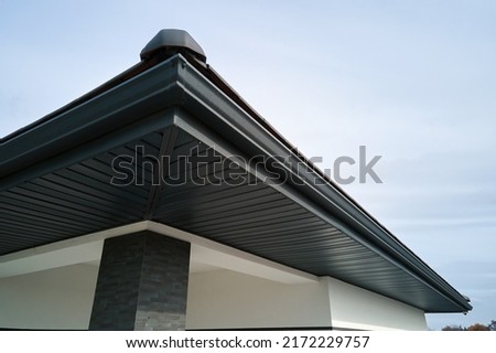 House corner with brown metal planks siding and roof with steel gutter rain system. Roofing, construction, drainage pipes installation