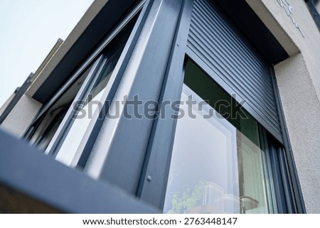 House corner window with partially closed roller shutter on exterior facade. Concept of home exterior, security and contemporary architectural detail