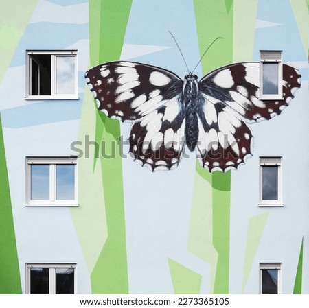 house detail of a modern apartment block, artistically designed with mural pattern of polygonal shapes symbolizing abstracted floral elements and a painted checkered butterfly, Langen, Germany