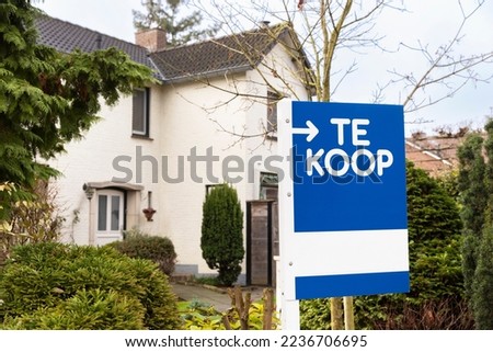 House exterior facade with a sign saying ' Te Koop', for sale. Housing market, selling or buying property, investing in real estate concept. Dutch home surrounded by trees and greenery during winter