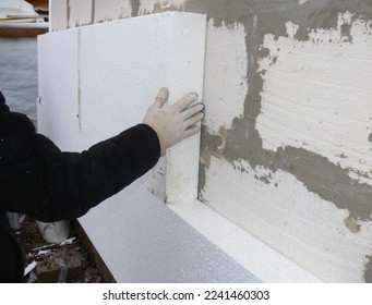 House exterior wall foam insulation. A close-up of a building contractor installing a rigid foam, styrofoam insulation on the concrete block house wall. - Shutterstock ID 2241460303