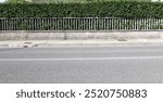 House fence consisting by a long  wall with concrete railing. Hedge on behind. Cement sidewalk and asphalt street in front. Background for copy space