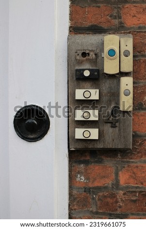 House front with 7 modern analog doorbells attached to a old worn wooden piece of wood with house number 4 attached