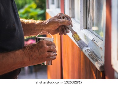 House Improvement. Senior Craftsperson Is Painting Wooden Window Frame Using Paintbrush. Old Man Working Outdoors.