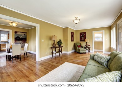 House Interior With Open Floor Plan. Room Furnished With Green Sofa And Armchair. View Of Dining Table Set In Kitchen Room