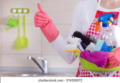 House Keeper Holding Basin Full Of Cleaning Supplies And Showing Thumb Up In Front Of Clean Kitchen