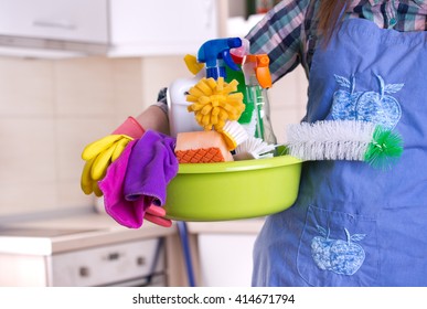 House Keeper Holding Basin Full Of Cleaning Supplies In Front Of Clean Kitchen