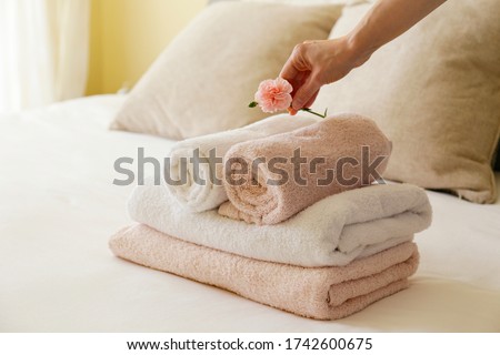 House keeping lady changing the set of folded and stacked towels in hotel room with freshly made bed, perfectly clean and ironed sheets in natural sun light. Close up, copy space for text.