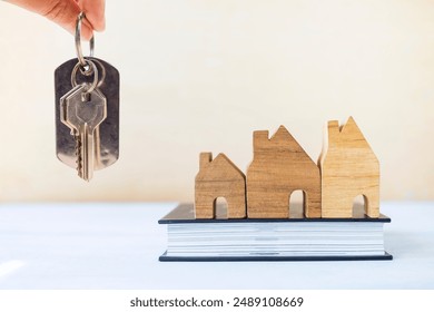 House key in girl hand with wooden house model on book with space on blurred background, property business, real estate investment - Powered by Shutterstock