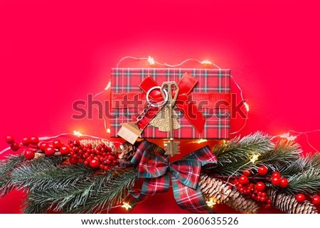 House key with keychain cottage on a festive background with Christmas tree, lights of garlands. Happy New Year-red background, gift, greeting card. Purchase, construction, relocation, mortgage