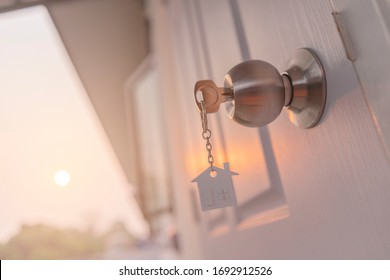 House key on house shaped keyring in the lock of door,Sunset background